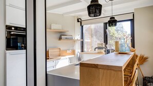 Een moderne keuken met witte kasten, een houten kookeiland, zwarte hanglampen en een groot raam dat voor natuurlijk licht zorgt.