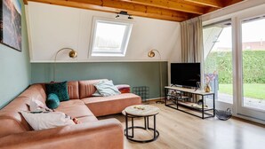 Un salon moderne avec un canapé en cuir, une table basse, un téléviseur posé sur un meuble et une grande fenêtre donnant sur l’extérieur.