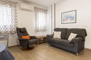 Uma sala de estar com um sofá cinza, uma poltrona cinza, uma pequena mesa de madeira e um quadro na parede.