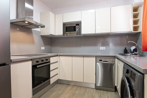 Eine kompakte Küche mit integrierten Geräten, darunter Mikrowelle, Backofen und Geschirrspüler, in modernem Design und mit einer neutralen Farbgebung.