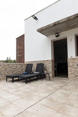 A covered outdoor seating area with two lounge chairs and a potted plant.
