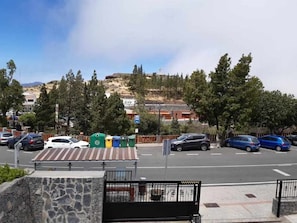 A parking area with multiple cars, a stone wall, and a view of a hilly landscape with trees and buildings in the background.