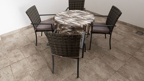 Une table ronde recouverte d’une nappe à motifs, entourée de quatre chaises en osier dotées de coussins.