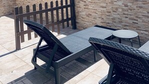 Un espace extérieur aménagé avec des chaises et une table en métal, un mur en pierre et une vue sur des bâtiments et des arbres.