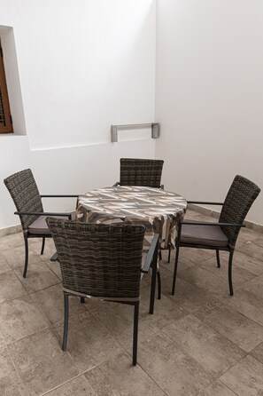 A round table with a patterned tablecloth surrounded by four wicker chairs.