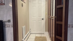 Um corredor com uma porta branca, um radiador, um tapete marrom e armários de madeira.