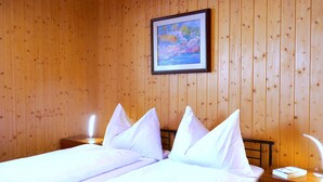 A double bed with white linens in a room with wooden panel walls.