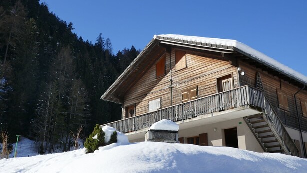 A wooden chalet with a balcony and a staircase leading to an upper level.
