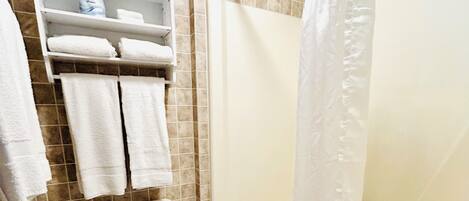 A bathroom with a toilet, a bathtub, and a shower curtain. There are towels hanging on a rack and a trash bin.
