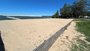 A sandy beach with a wooden fence and benches, a clear blue sky, and trees in the background. - Silver Sands Hotel & Resort (Mears)