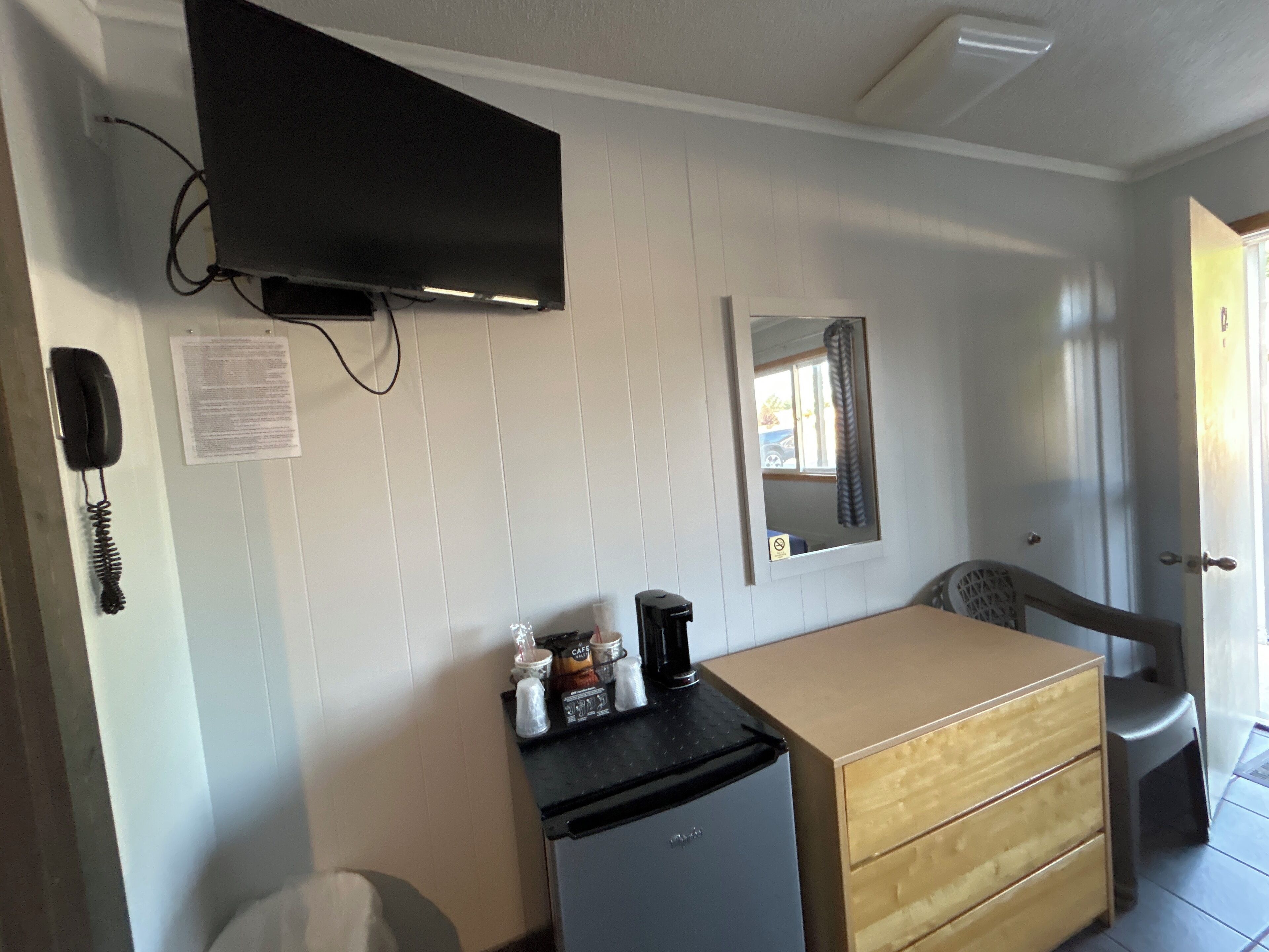 Habitación de hotel compacta con una cama individual, un escritorio pequeño con silla, televisor montado en la pared, teléfono y espejo.