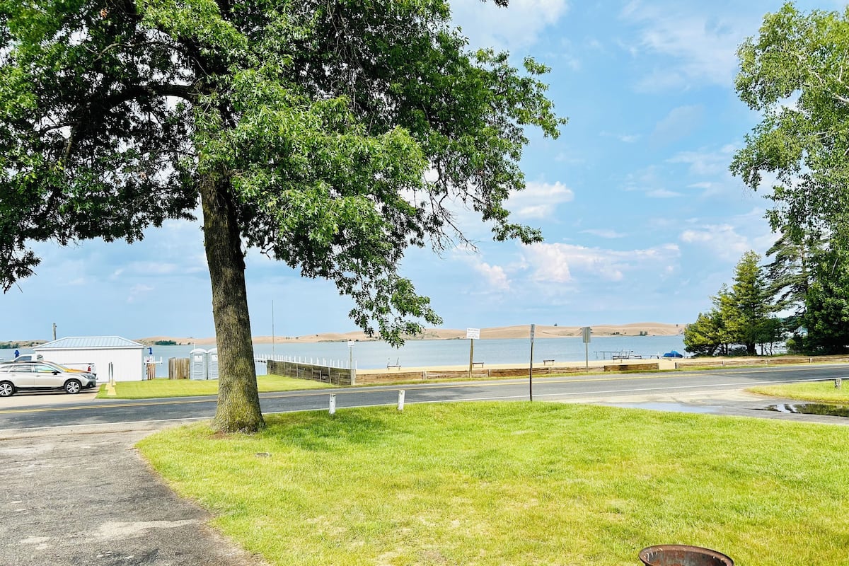 A parking area with a tree, a grassy field, and a view of a body of water.