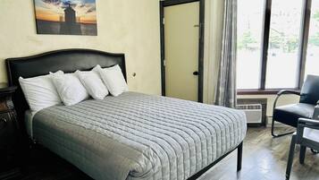 A neatly made bed with a grey quilt, a dark headboard, and white pillows. A painting of a sunset over a pier is on the wall.