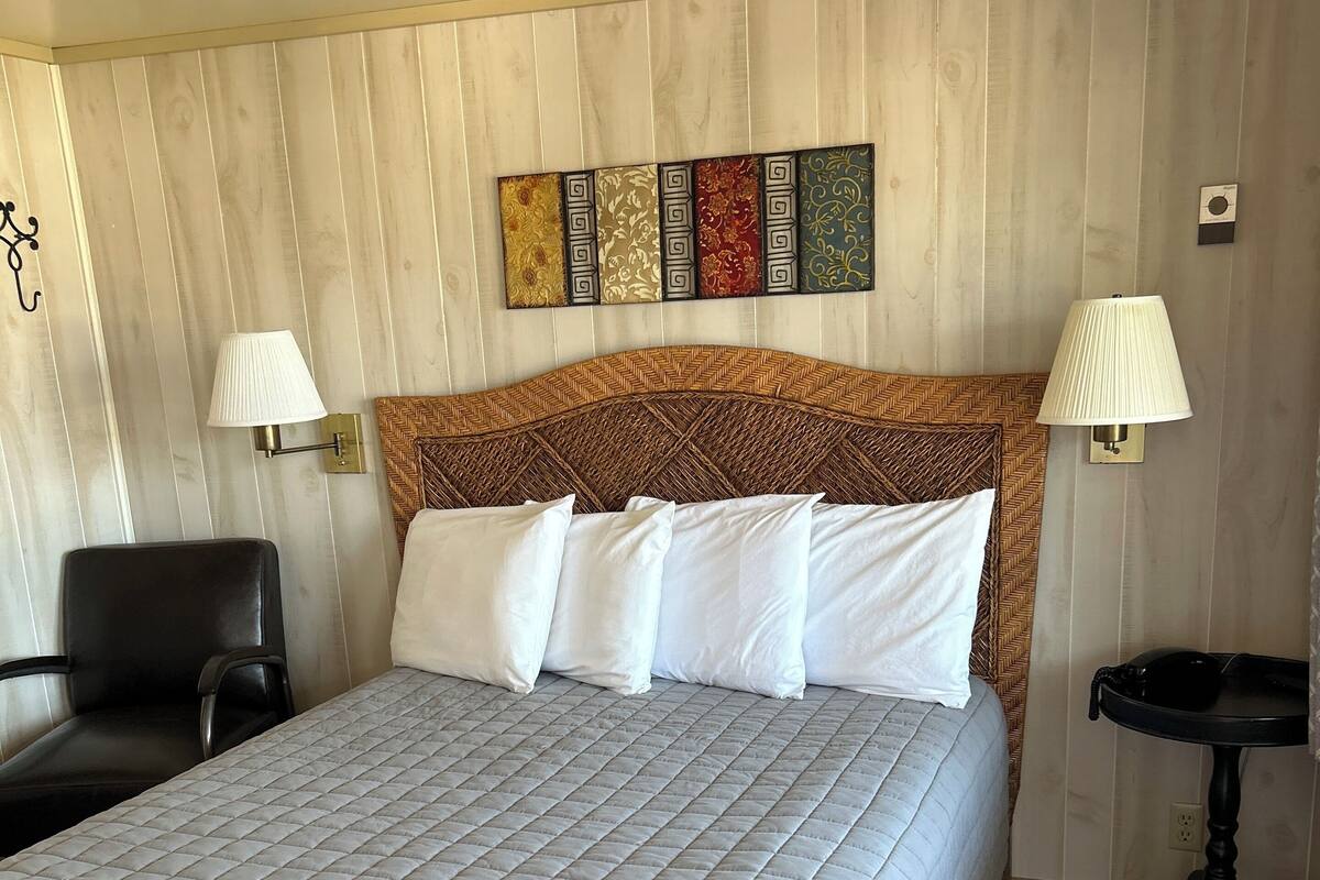 A hotel room with a large bed, two bedside lamps, a chair, a small table, and a decorative wall panel.