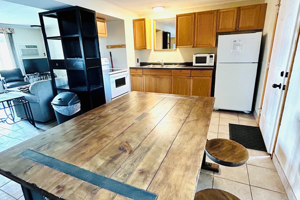 A kitchen with wooden cabinets, a white refrigerator, a microwave, and a dining table with stools.