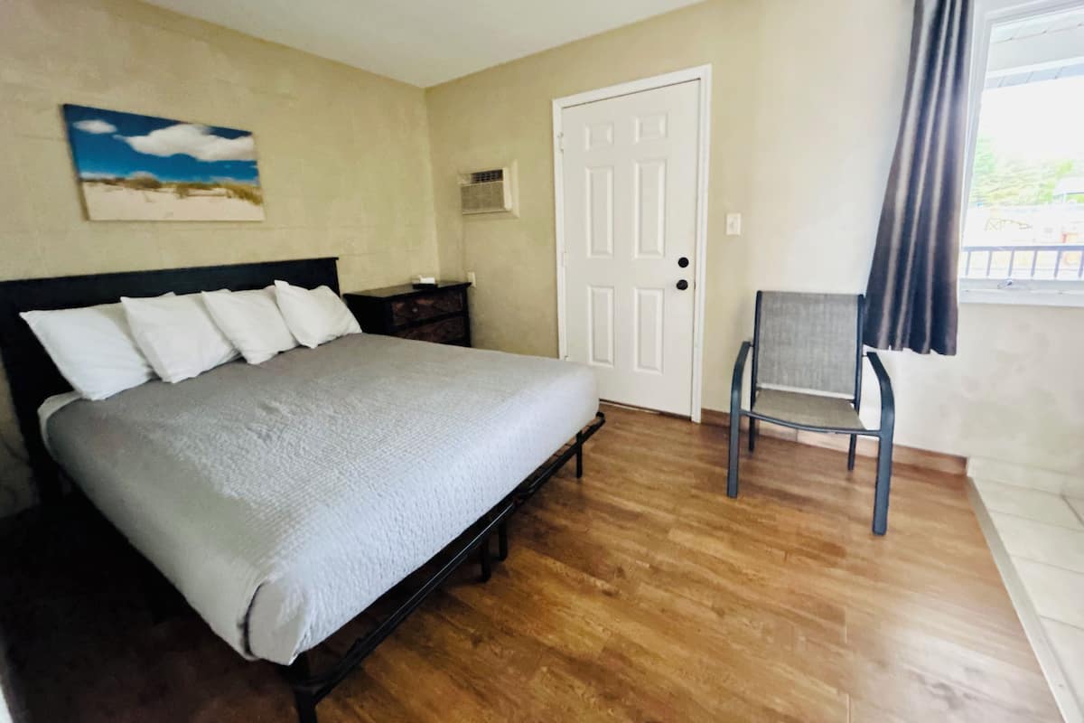 A bedroom with a bed, a chair, a door, and a window with curtains.