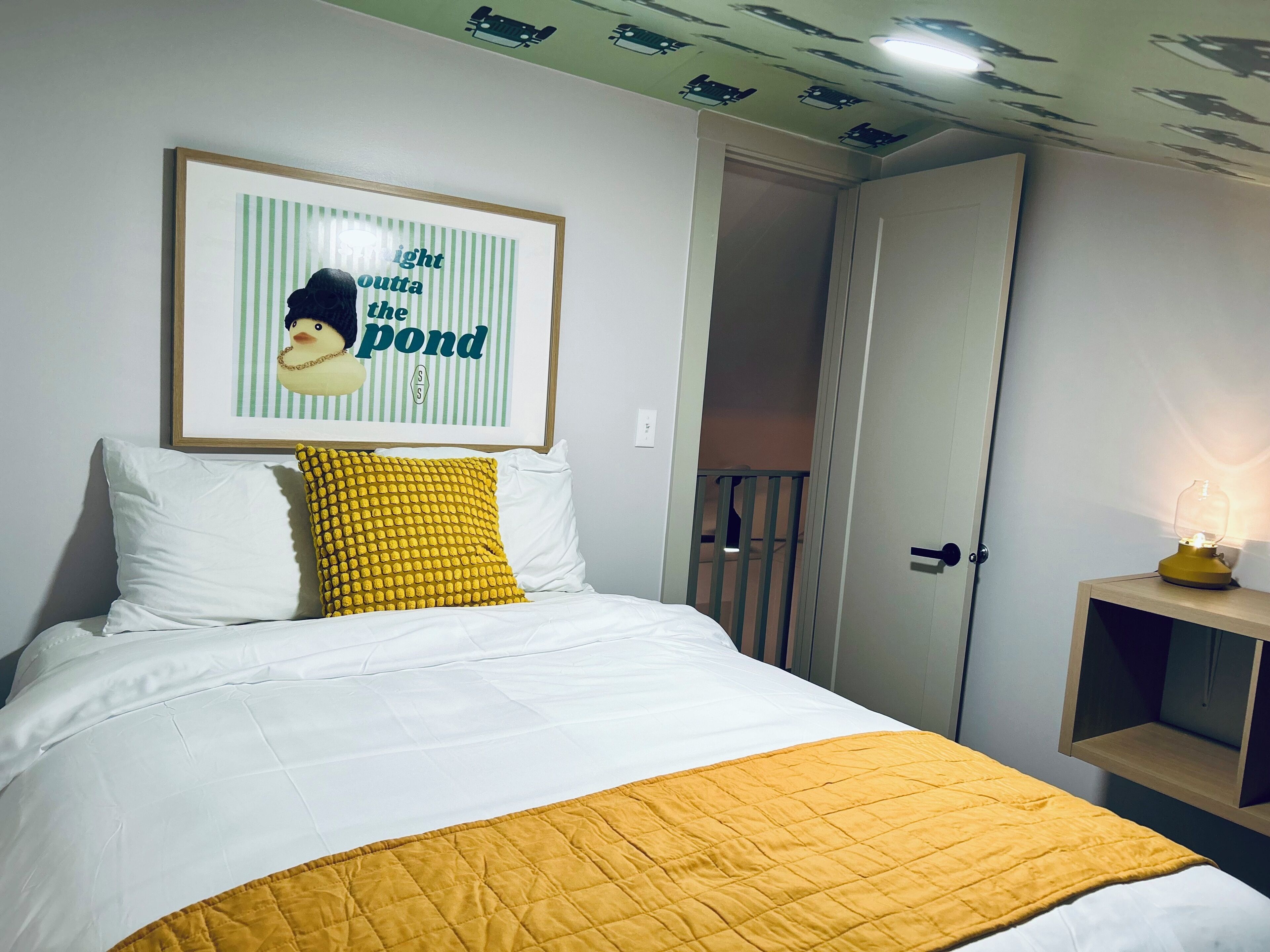 A bed with white and yellow bedding, a framed picture above it, and a door to a balcony.