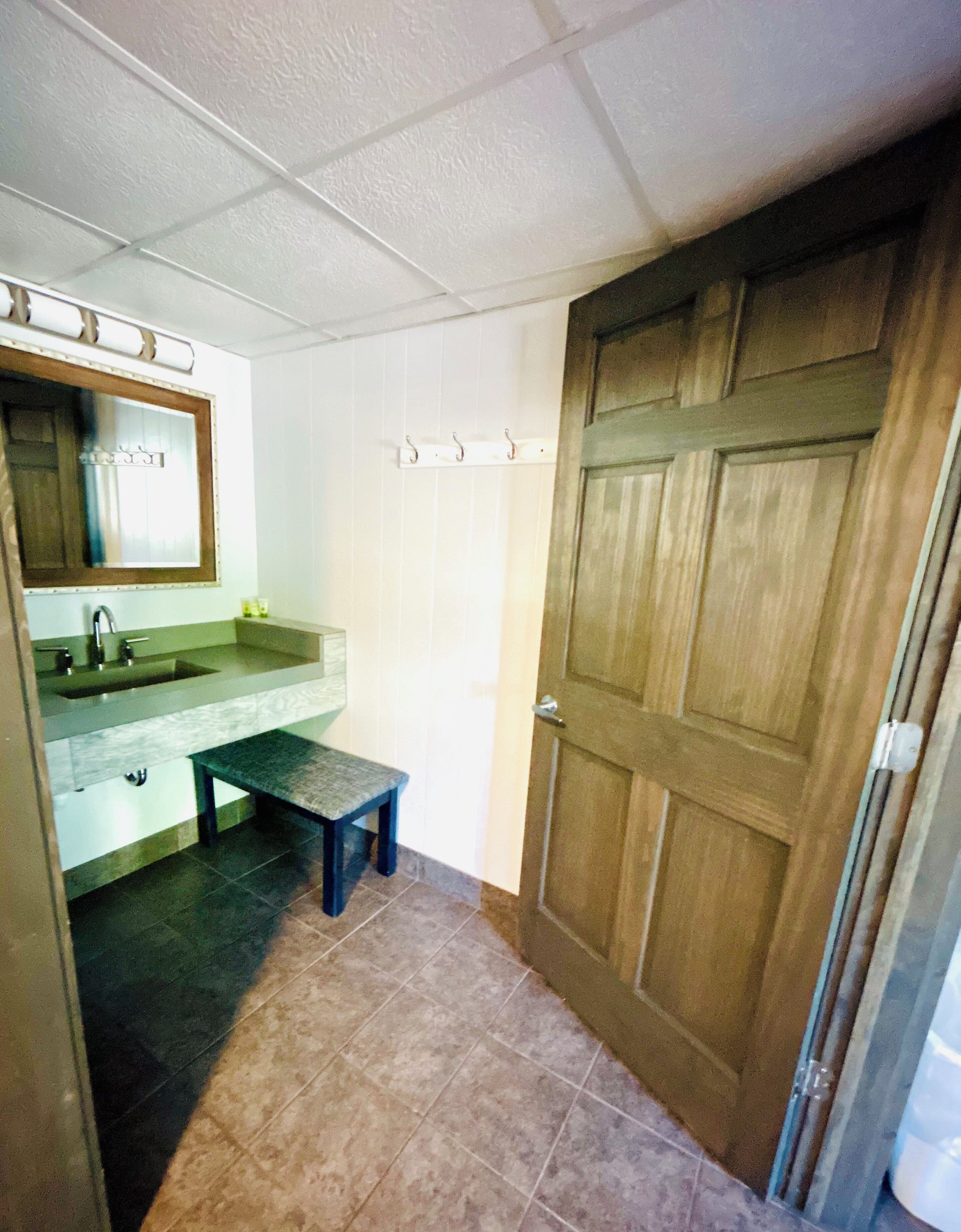 Une salle de bain avec un lavabo, un miroir, un banc et une porte en bois.