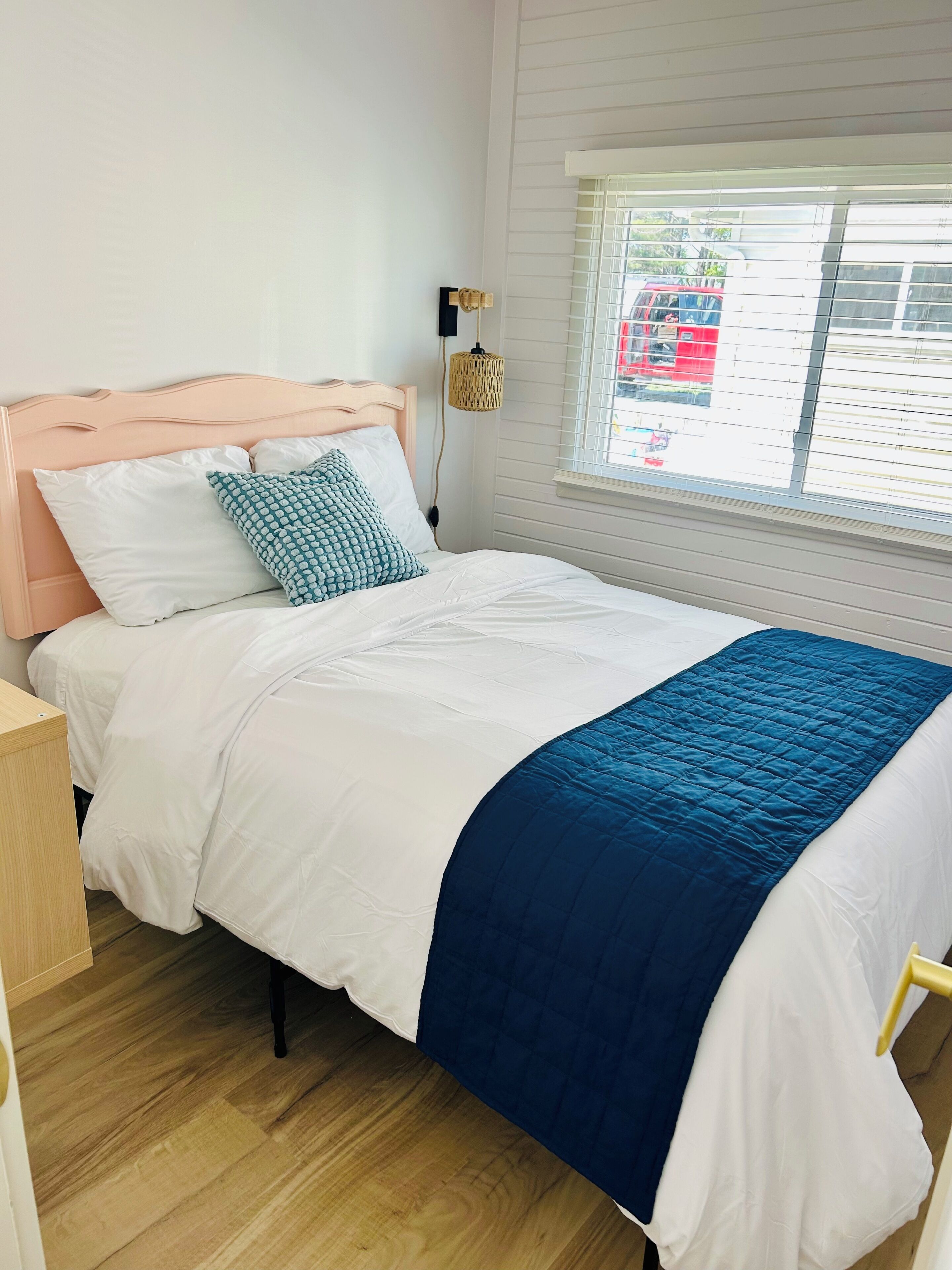 A bed with a wooden headboard, white bedding, and a blue quilt.