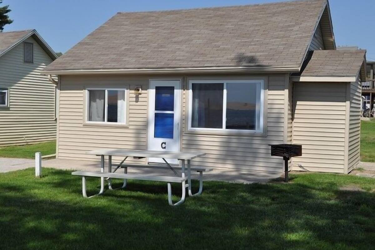 A small, single-story building with a sloped roof, a front door, and a picnic table in front.