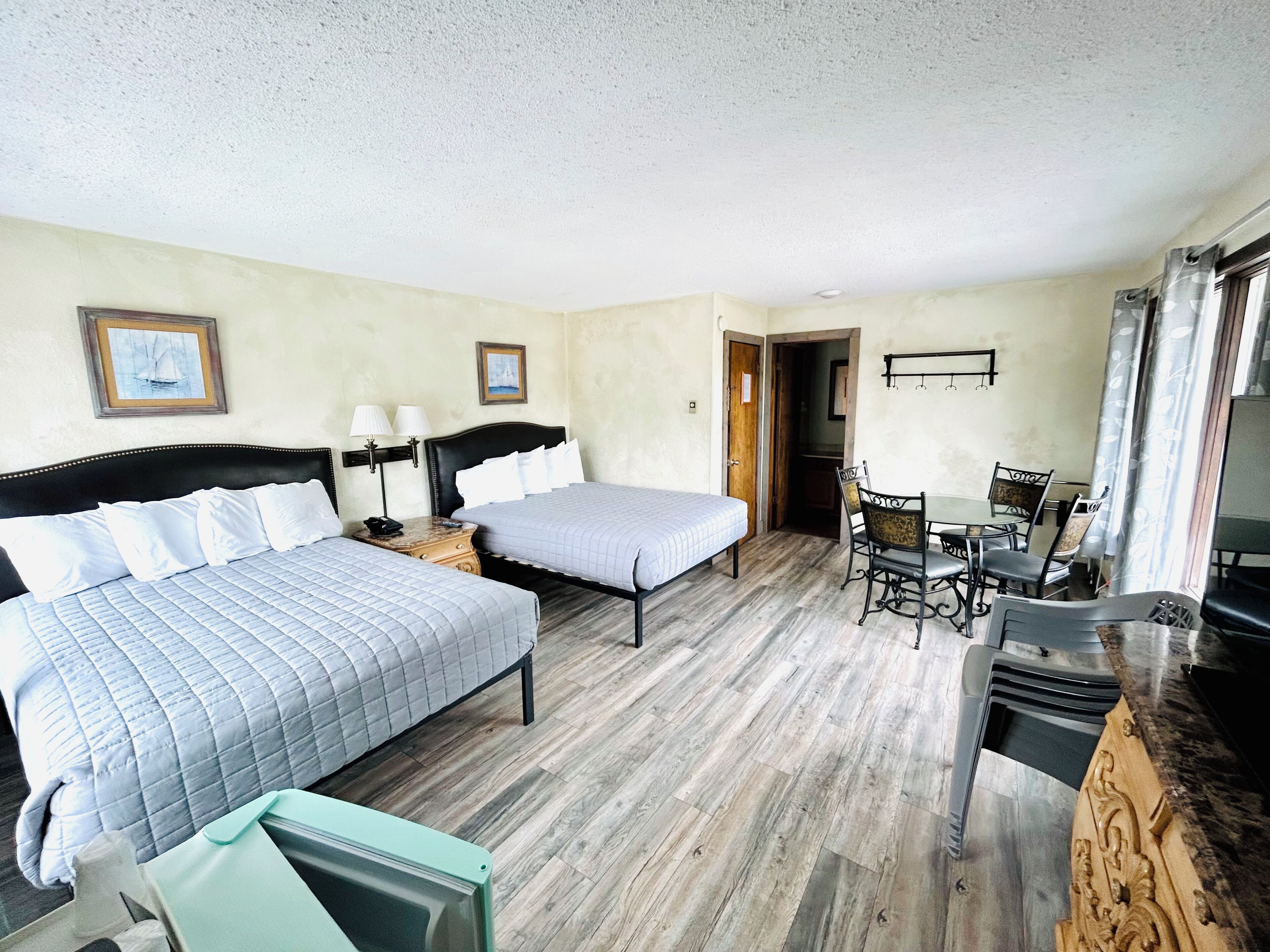 A hotel room with two beds, a dining table with chairs, a TV, and a wooden floor.