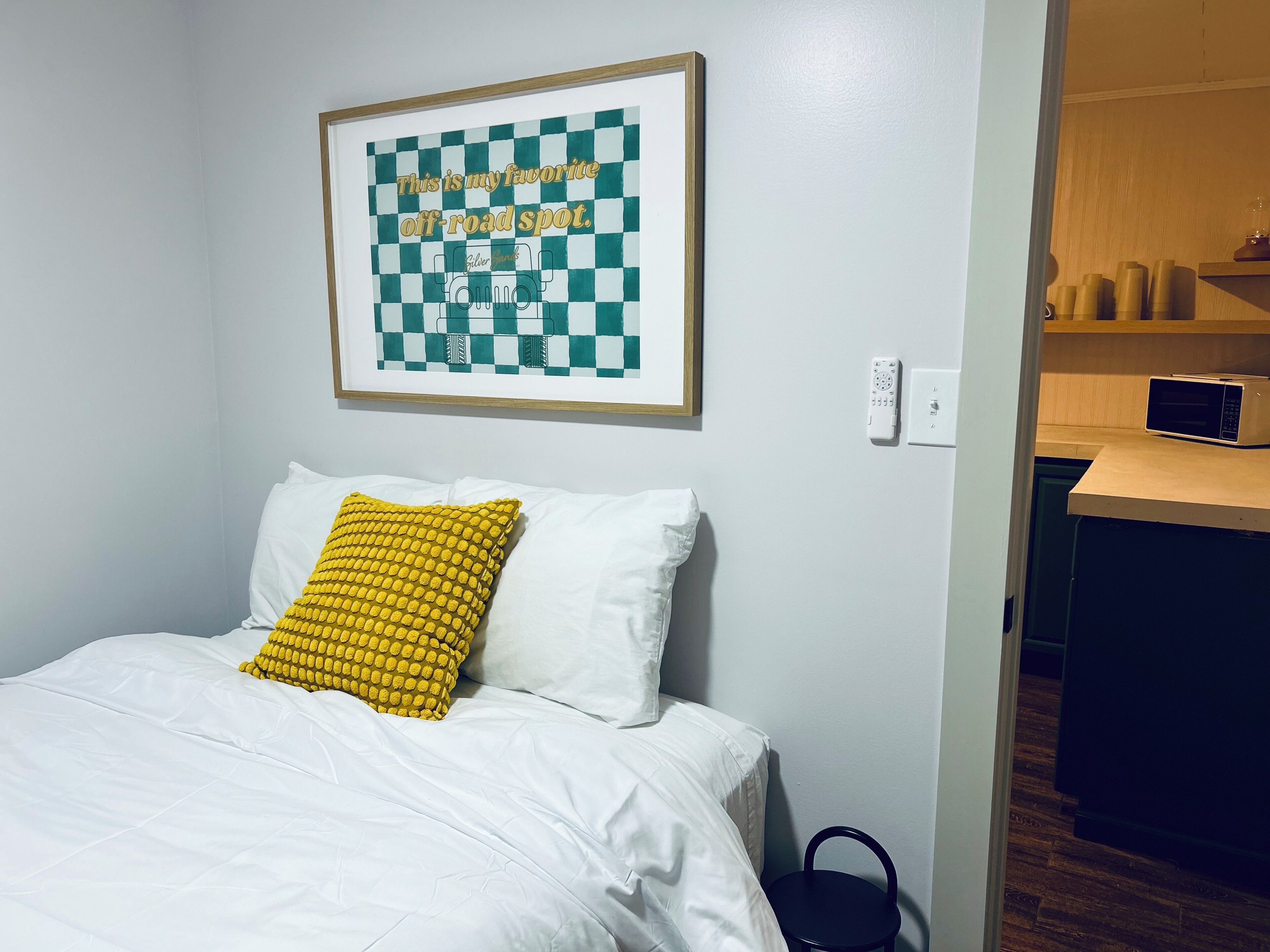 A room with a bed, a framed quote on the wall, a microwave, and a small kitchen area.