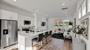 A modern kitchen with white cabinetry, a stainless steel refrigerator, a microwave, and a large island with bar stools. - Stylish Two Story Close to South End and Uptown (Charlotte)
