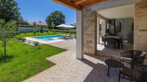 A covered outdoor area with a pool, seating, and a view of the backyard.