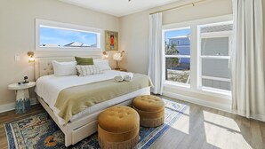 A bedroom with a bed, two ottomans, a ceiling fan, a nightstand, a rug, and a window with curtains. - New Listing! Luxury Beachside Townhouse GR8 Views! (Mexico Beach)
