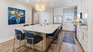 A modern kitchen with a central island, bar stools, and a large painting on the wall. - New Listing! Luxury Beachside Townhouse GR8 Views! (Mexico Beach)