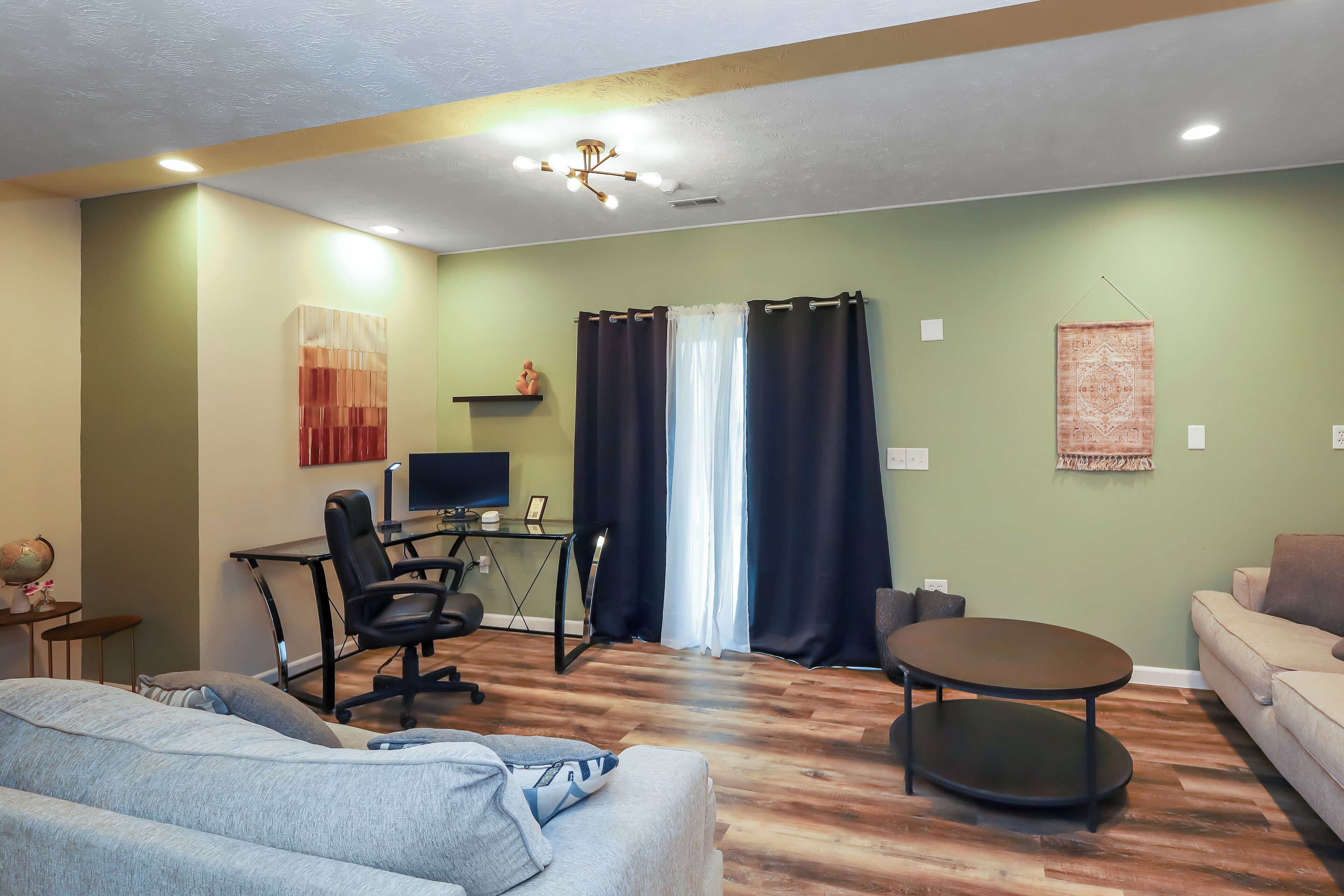 A living room with a sofa, a coffee table, a desk with a computer, and a TV.
