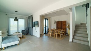 Un vaste espace de vie comprenant un canapé, une table à manger avec des chaises, un téléviseur fixé au mur et un escalier menant à l’étage supérieur.