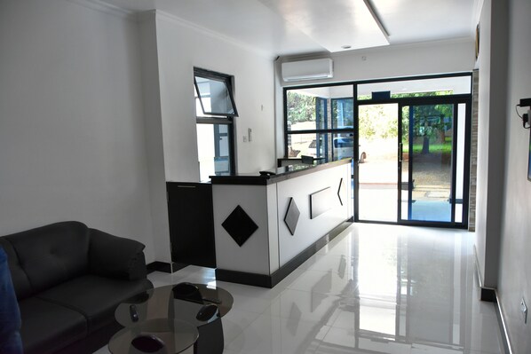 A modern hotel lobby with a reception desk, a sofa, and a glass coffee table. - Alexandrina's Corner Bed and Breakfast (Chipata)