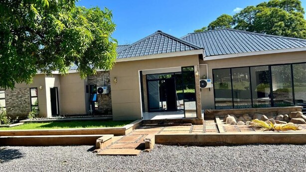 A modern building with a sloped roof, large windows, and a gravel driveway. - Alexandrina's Corner Bed and Breakfast (Chipata)