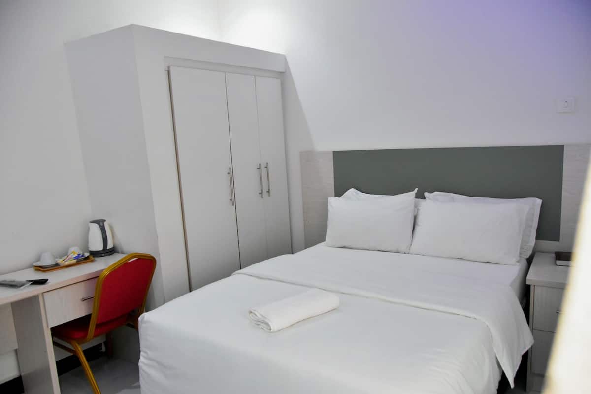 A hotel room with a bed, a desk, a chair, and a wardrobe.