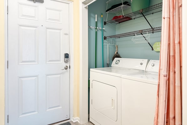 A laundry room with a white washing machine, a drying rack, and a door.