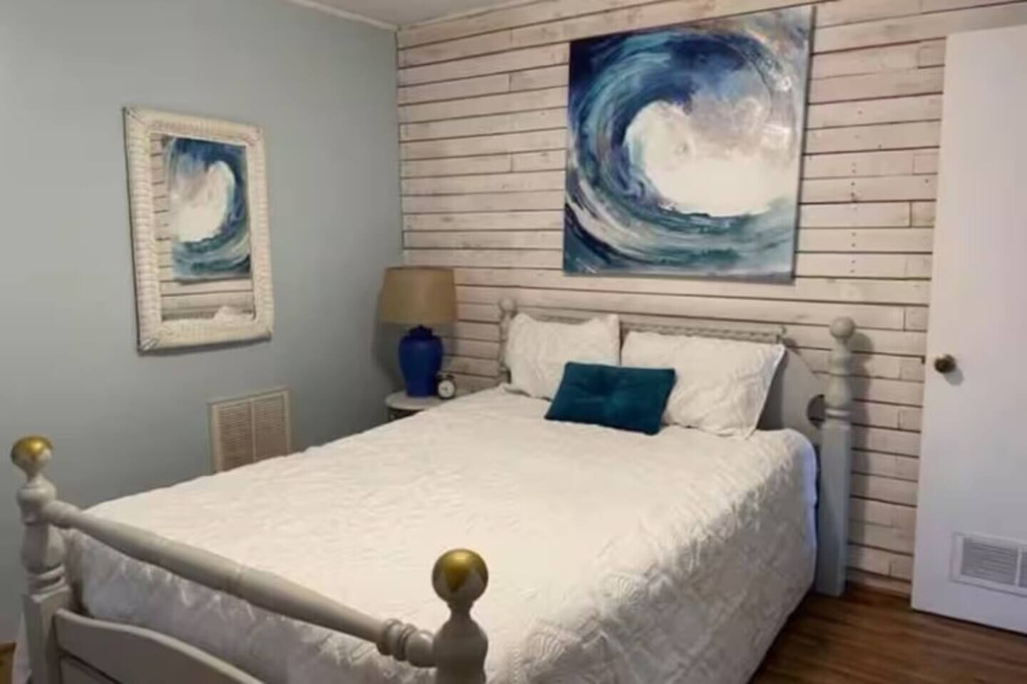 Ein Schlafzimmer mit einem Bett, einem Nachttisch, einer Lampe und zwei Bildern an der Wand.