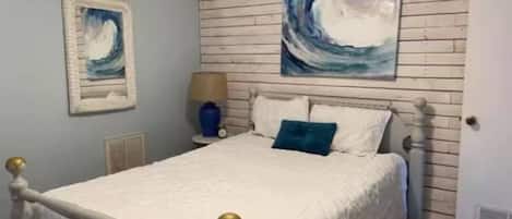 Une chambre à coucher avec un lit, une table de chevet, une lampe et deux tableaux au mur.