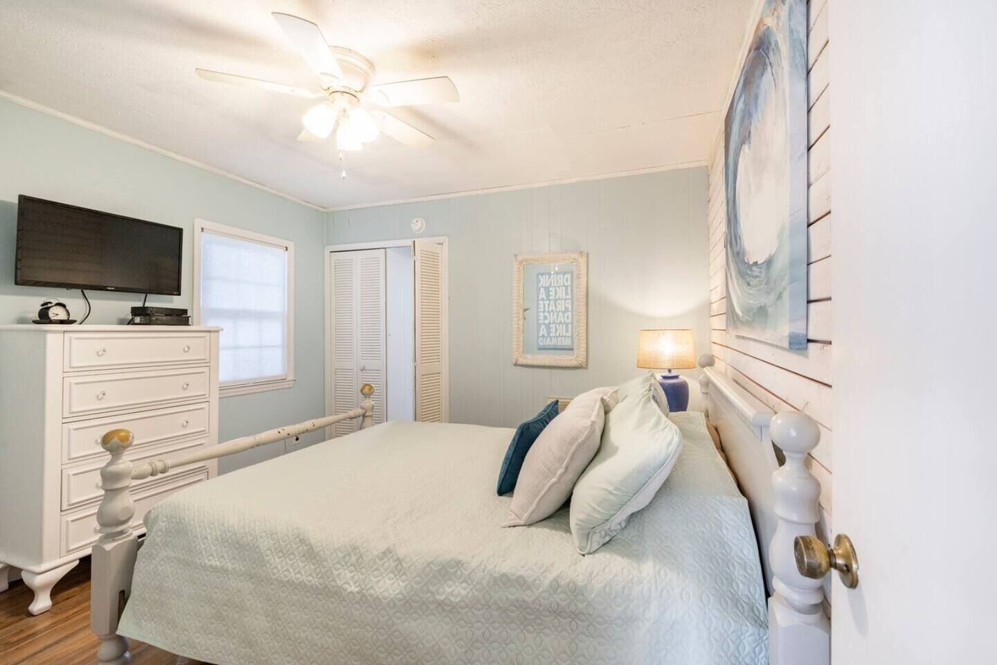 A bedroom with a bed, dresser, television, and a ceiling fan.