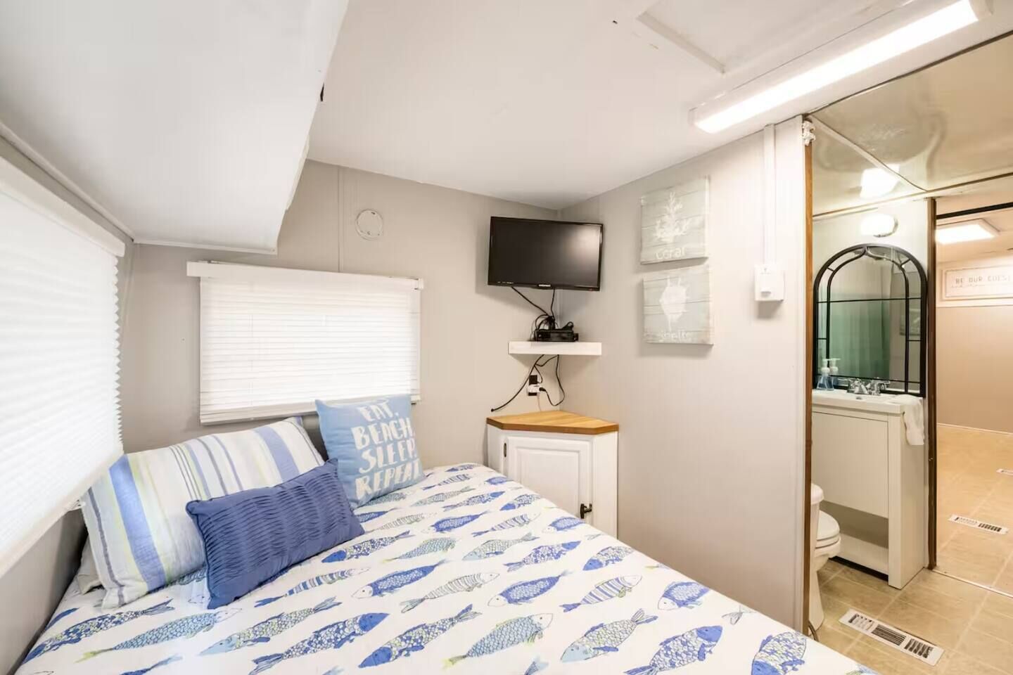 Un dormitorio con cama, televisión, un mueble pequeño y baño con lavabo y espejo.