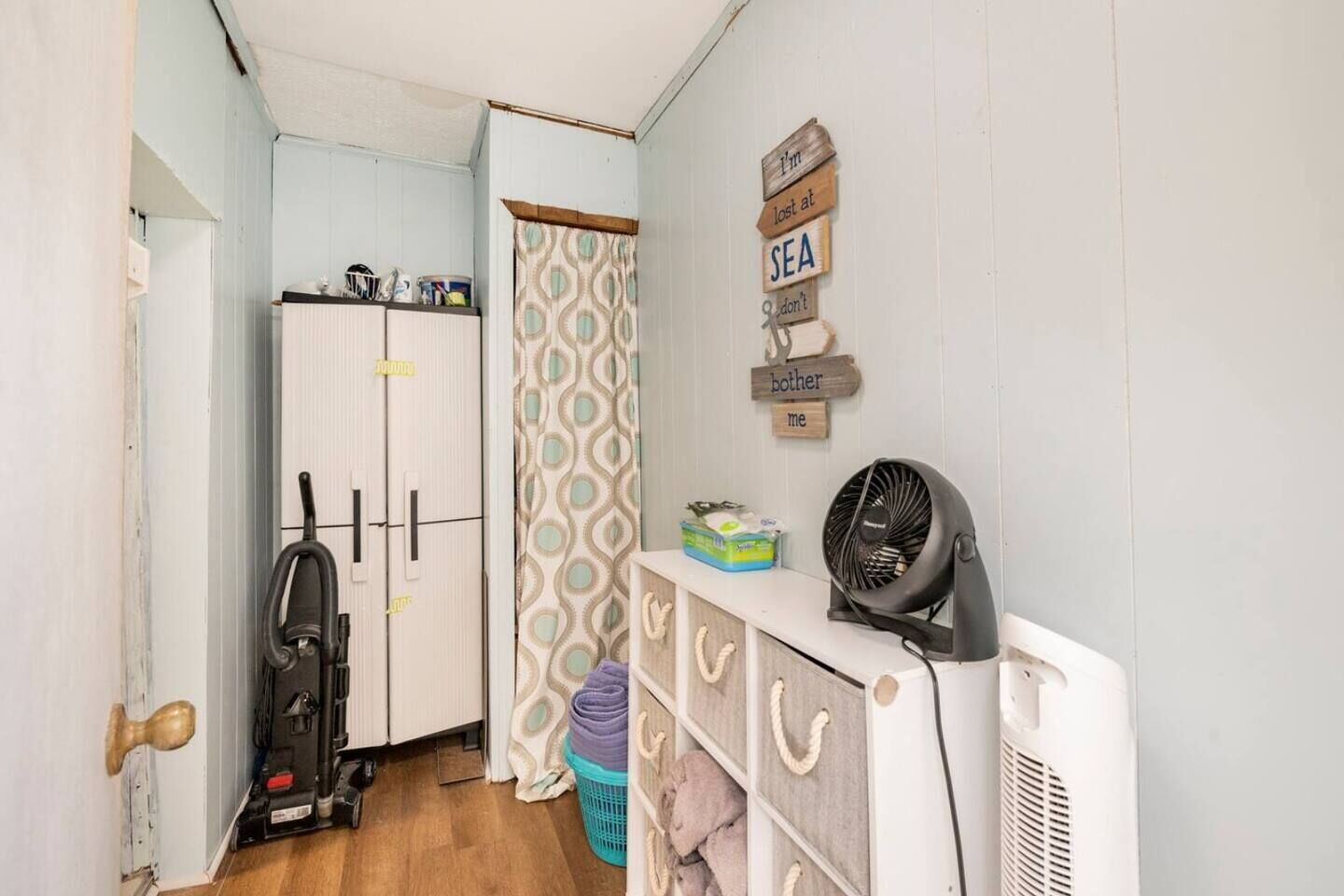 A compact room with a white radiator, a vacuum cleaner, a fan, and a laundry basket.