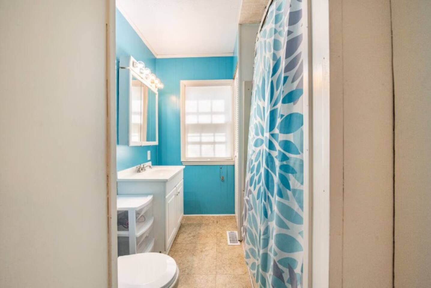 Ein Badezimmer mit blauer Wand, weißem Waschbecken und einer Duschvorhang mit Blätermuster.