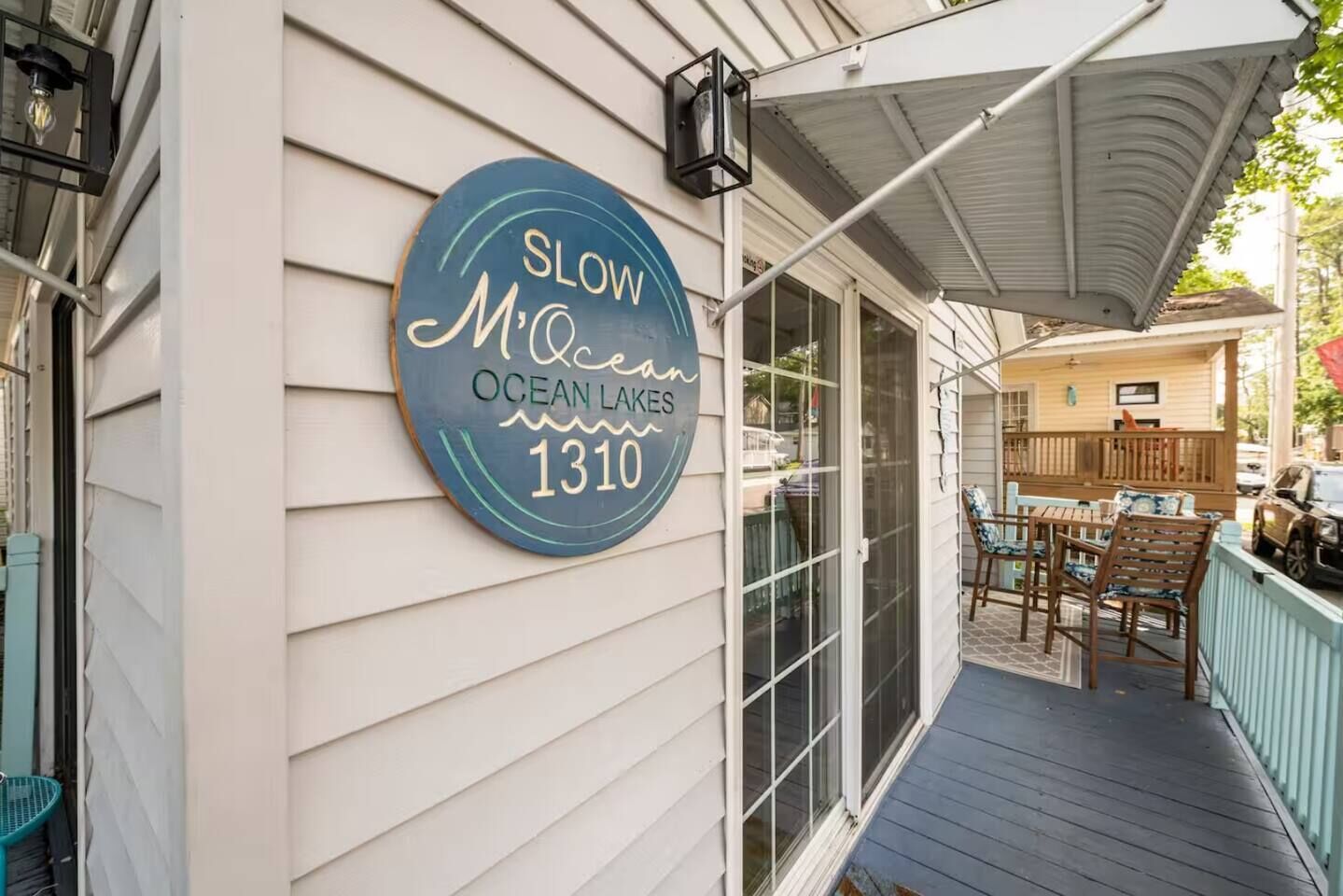 Una casa con un porche, un cartel que dice "SLOW M'OCEAN OCEAN LAKES 1310" y muebles de exterior.