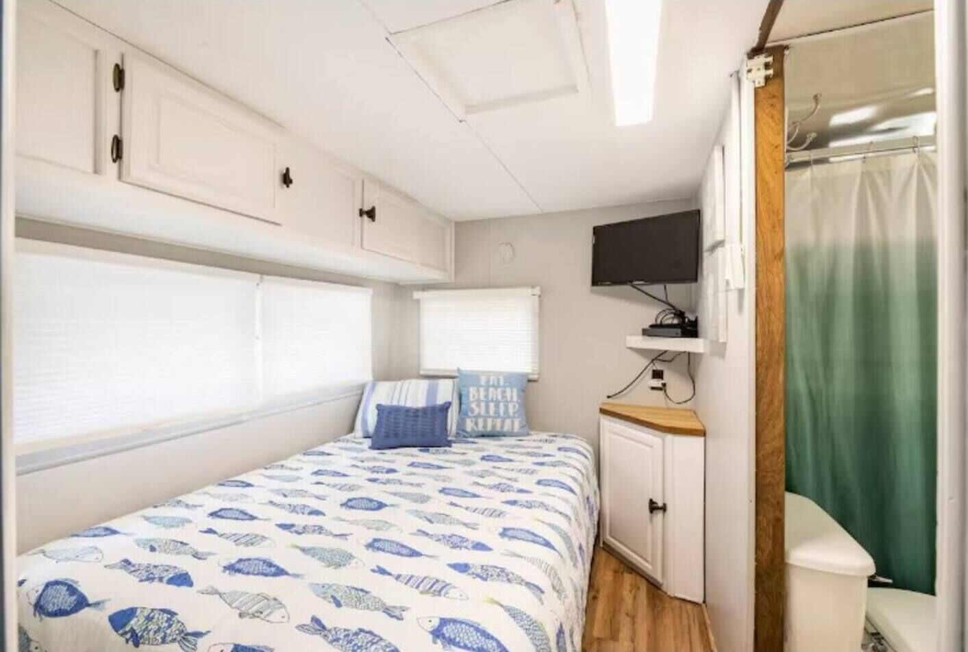 Ein kleines Schlafzimmer in einem Wohnmobil mit Bett, einem kleinen Schrank, einem Fernseher und einem Duschbereich.