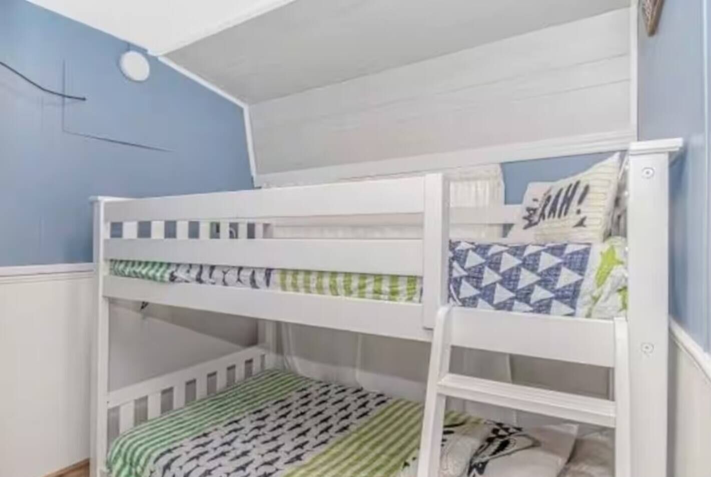 Ein Etagenbett mit zwei Schlafstellen, jeweils mit Kopfkissen und einer gemusterten Decke.
