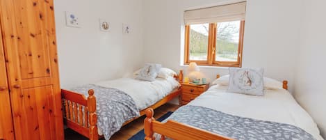 Un dormitorio con dos camas individuales, un armario de madera, una mesita de noche con lámpara y una ventana con vistas al verdor.