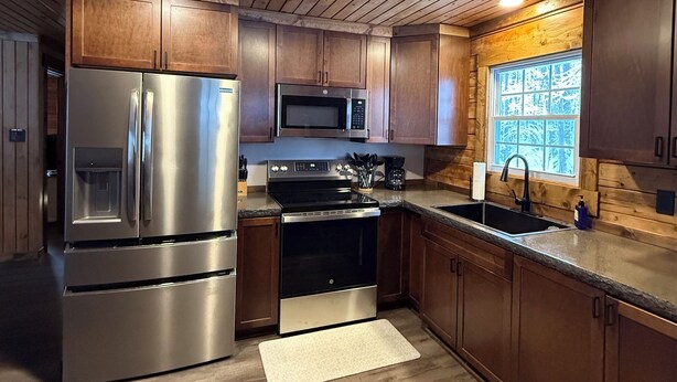 A modern kitchen with wooden cabinets, stainless steel appliances, and a window with a view of trees.