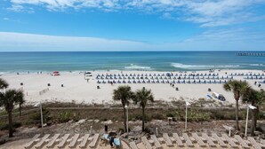 A beach with rows of sun loungers, a pier in the distance, and a clear sky. - Calypso 404E, VIP Parking Spot, Beach Chairs! (Panama City Beach)