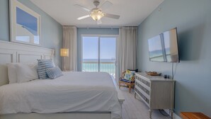 A bedroom with a bed, a ceiling fan, a dresser, a TV, and a view of the ocean. - Calypso 404E, VIP Parking Spot, Beach Chairs! (Panama City Beach)