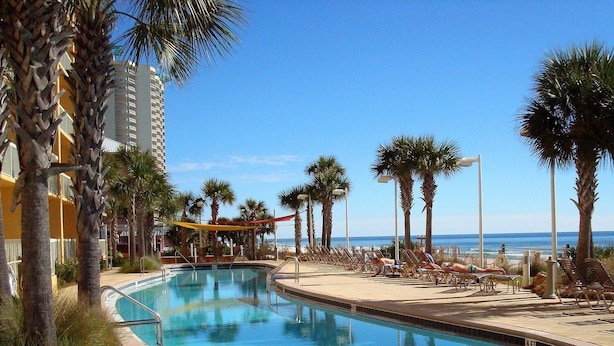 A pool area with a clear view of the ocean, surrounded by palm trees and lounge chairs. - Calypso 404E, VIP Parking Spot, Beach Chairs! (Panama City Beach)